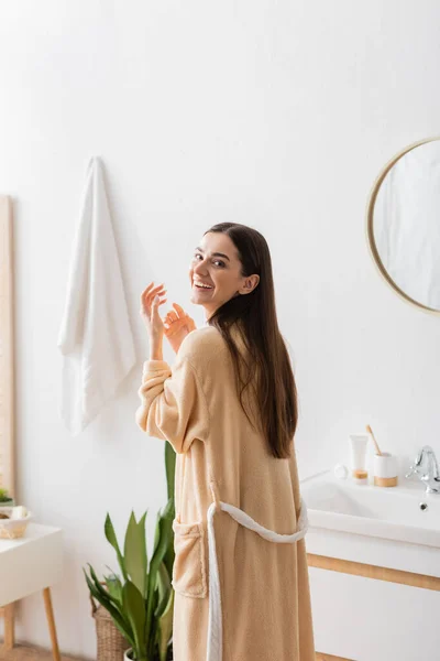 Positive woman in bathrobe looking at camera and laughing in bathroom — Stock Photo