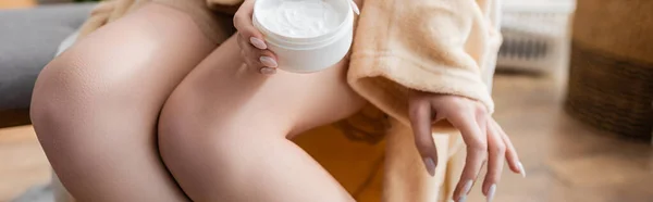 Cropped view of young woman in bathrobe holding cosmetic cream at home, banner — Stockfoto