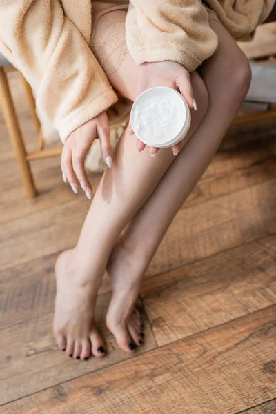 Cropped view of woman in bathrobe holding body cream at home in morning — Stock Photo