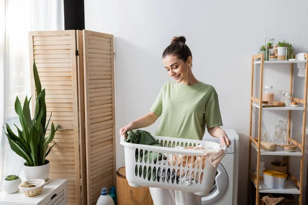 Smiling young woman holding basket with laundry at home - foto de stock