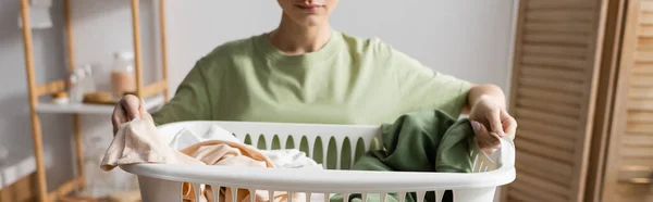 Cropped view of blurred woman holding basket with clothes in laundry room, banner - foto de stock