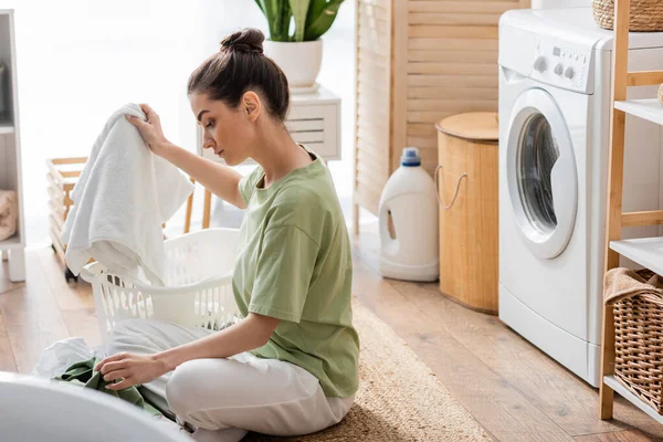 Seitenansicht einer brünetten Frau, die Kleidung in der Waschküche sortiert — Stockfoto