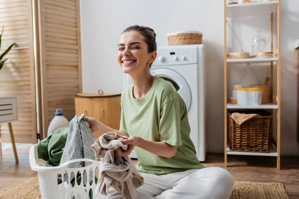Happy young woman holding clothes in laundry room — Fotografia de Stock