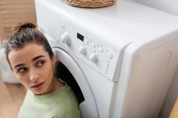 Брюнетка смотрит на стиральную машину в прачечной — стоковое фото
