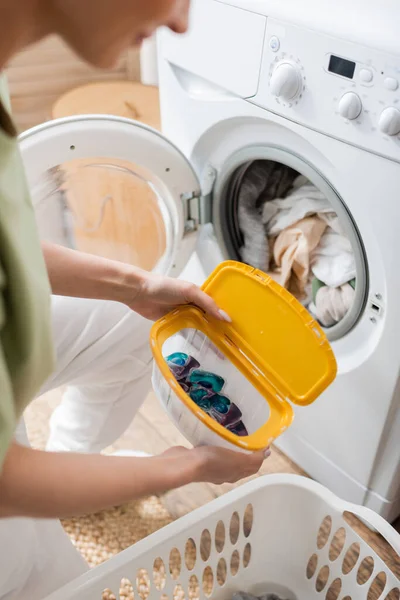 Cropped view of woman holding box with washing capsules in laundry room — Fotografia de Stock