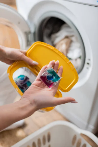 Cropped view of woman holding detergent pod and box near machine in laundry room — Stock Photo