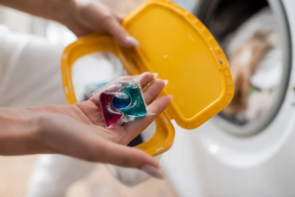 Cropped view of woman holding washing capsule and blurred box in laundry room — Stock Photo