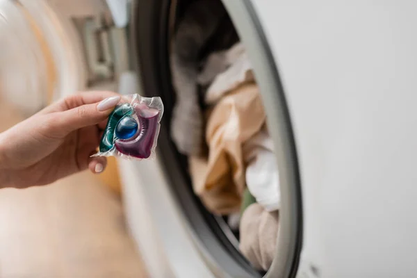 Vista cortada da mulher segurando vagem detergente perto da máquina de lavar roupa em casa — Fotografia de Stock