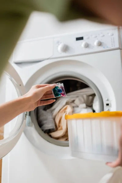 Vista recortada de la mujer que sostiene la cápsula de detergente cerca de la lavadora con lavandería - foto de stock