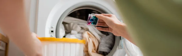 Vista cortada da mulher segurando vagem detergente perto da máquina de lavar roupa, banner — Fotografia de Stock