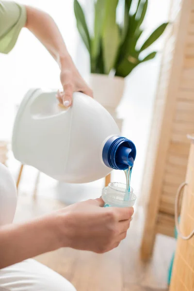 Cropped view of woman pouring liquid detergent in laundry room — Photo de stock