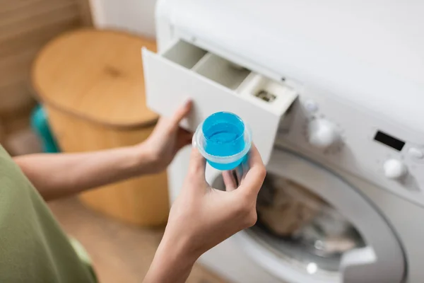 Cropped view of woman holding cap with blue washing liquid near machine in laundry room — Foto stock