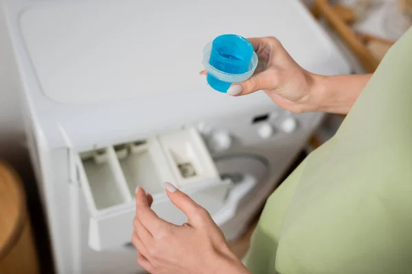 Cropped view of woman holding washing liquid near blurred machine in laundry room — Foto stock
