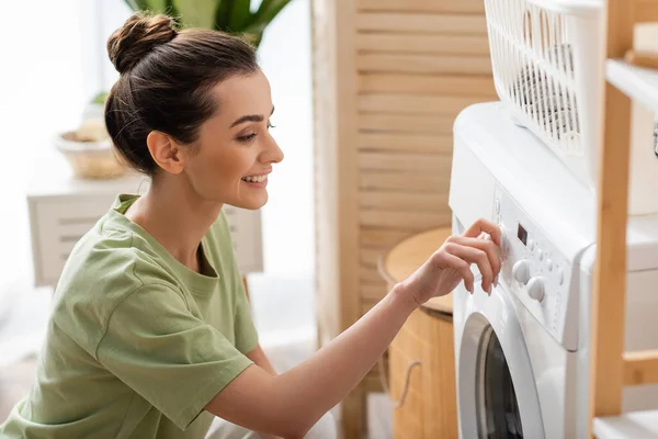 Positive young woman switching washing machine at home - foto de stock