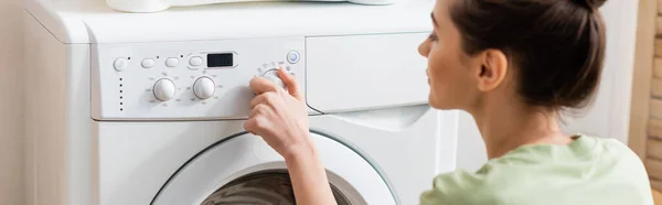 Вид збоку молодої жінки, що перемикає пральну машину вдома, банер — Stock Photo