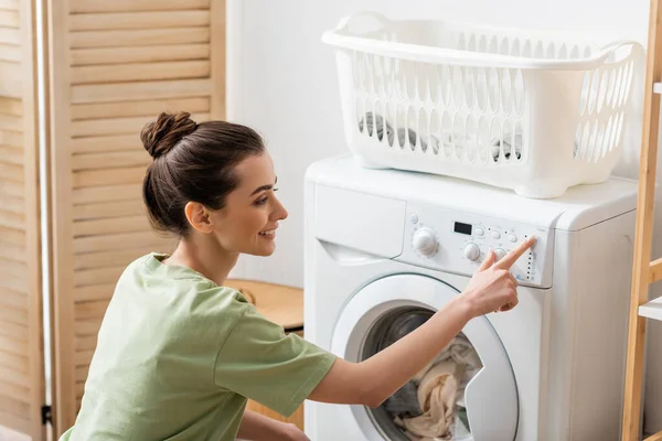 Side view of young woman switching washing machine at home - foto de stock