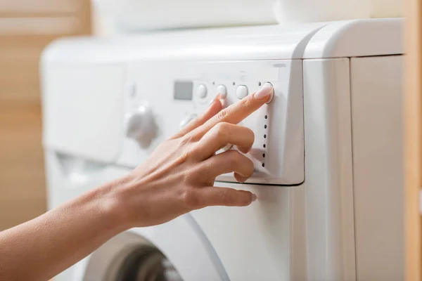 Vista cortada da mulher sintonizando máquina de lavar roupa branca na lavanderia — Fotografia de Stock