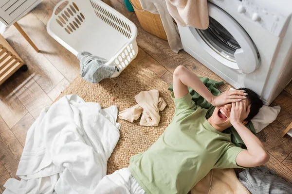 Ansicht von oben: Junge Frau verdeckt Augen und schreit in der Nähe von Kleidung auf dem Boden in der Waschküche — Stockfoto