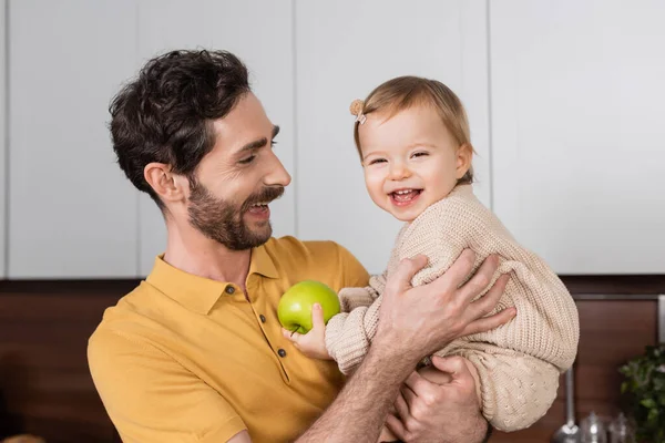 Sorrindo pai segurando criança filha com maçã na cozinha — Fotografia de Stock