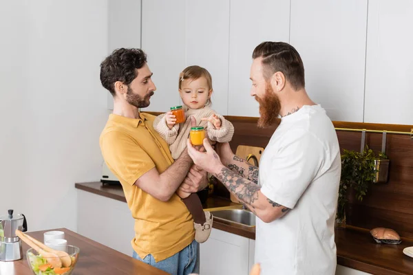 Отец-гей держит детское питание рядом с дочерью и партнером дома — стоковое фото