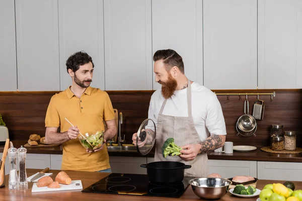 Familia del mismo sexo cocinar verduras y hacer ensalada juntos en la cocina - foto de stock