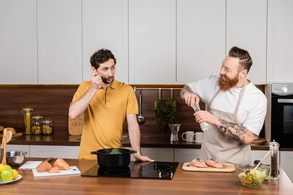 Coppia gay che cucina verdure e filetto di pollo in cucina — Foto stock