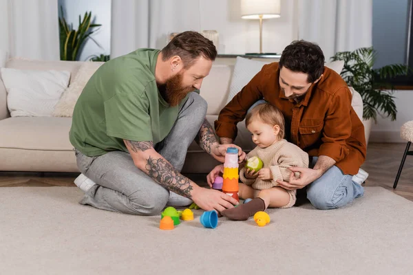 Mismo sexo padres jugando con bebé hija holding manzana en casa - foto de stock