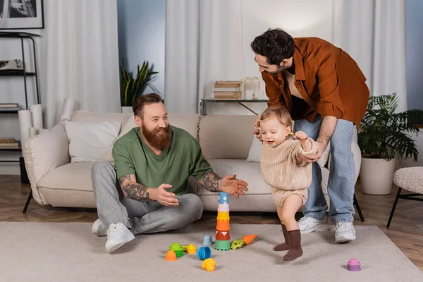 Веселі гомосексуальні батьки грають з дочкою у вітальні — стокове фото