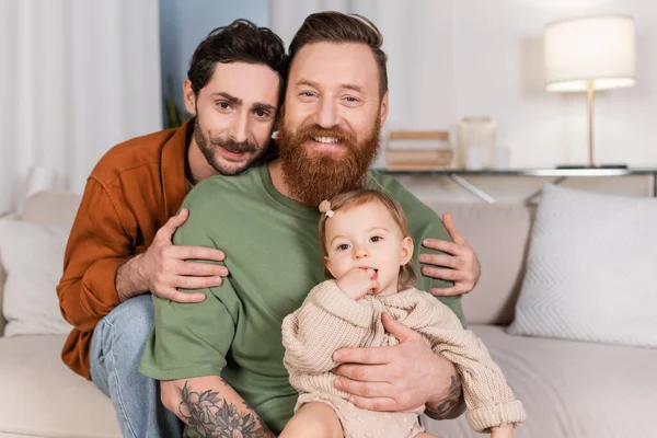 Smiling gay man hugging partner with baby daughter at home — Stock Photo