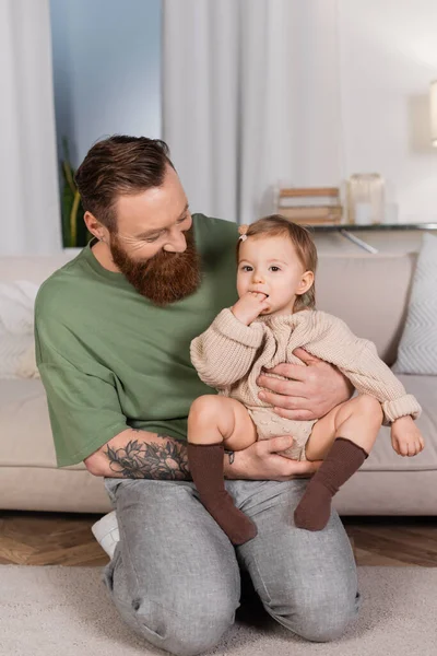 Bearded father holding baby daughter in living room — Photo de stock