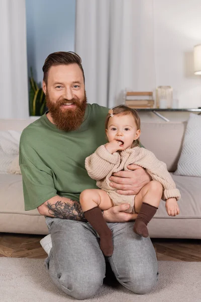 Cheerful tattooed dad holding baby girl at home - foto de stock