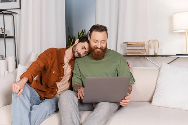 Gay couple using laptop on couch at home - foto de stock