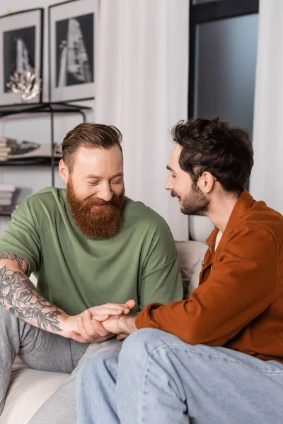 Smiling same sex couple holding hands on couch in living room — Stock Photo