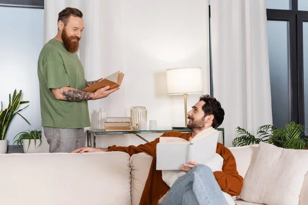 Sonriendo pareja del mismo sexo sosteniendo libros en la sala de estar - foto de stock