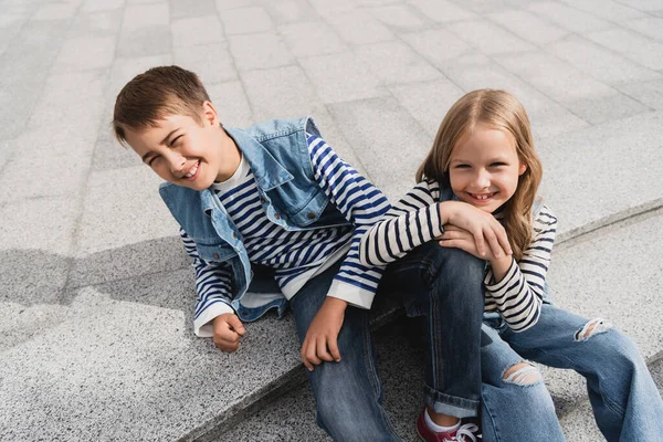 Blick aus der Vogelperspektive auf glückliche und gut gekleidete Kinder, die auf Treppen in der städtischen Straße sitzen — Stockfoto