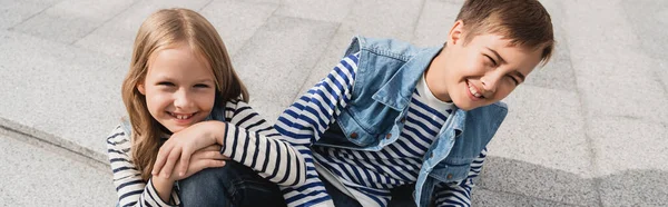 Vue grand angle des enfants heureux et bien habillés assis sur les escaliers dans la rue urbaine, bannière — Photo de stock