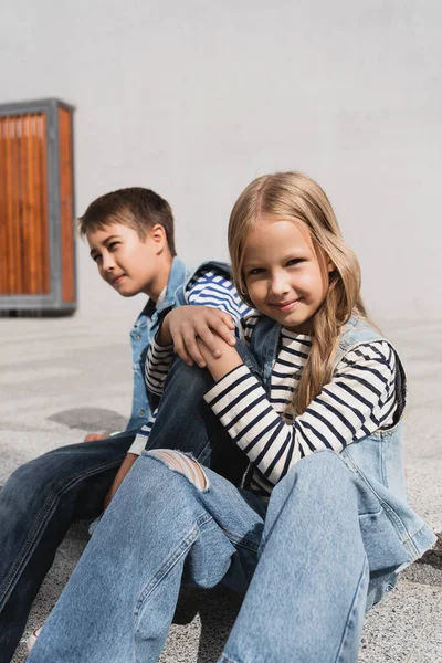 Menina bem vestida e alegre em colete jeans sentado perto de menino elegante — Fotografia de Stock