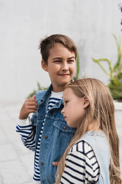 Preteen kid leaning on shoulder of boy in vest and striped long sleeve shirt - foto de stock