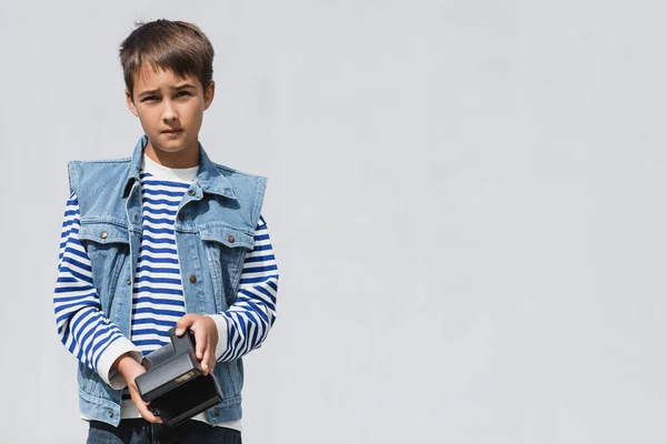 Well dressed preteen boy in denim clothes holding vintage camera on grey background — Fotografia de Stock