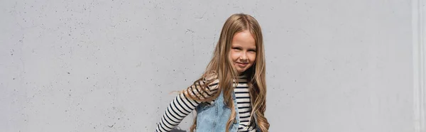 Весела дівчина в джинсовому жилеті смугаста сорочка з довгим рукавом, що стоїть біля сірої стіни, банер — стокове фото