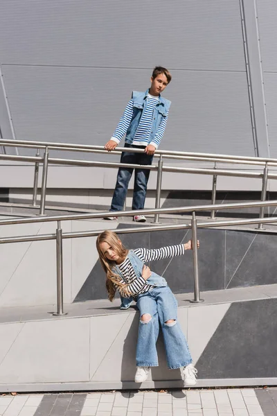 Bambini ben vestiti in abbigliamento casual denim posa vicino corrimano metallici accanto all'edificio — Foto stock