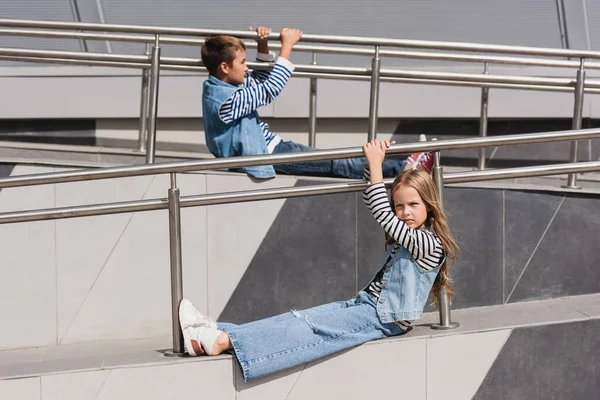 Well dressed kids in casual denim attire sitting near metallic handrails next to building — Stock Photo
