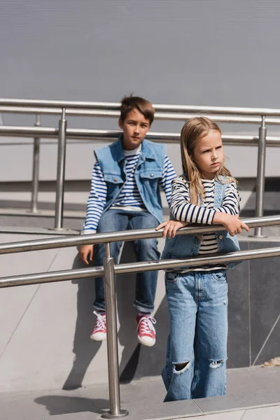 Well dressed children in casual denim attire posing near metallic handrails next to building — Stockfoto