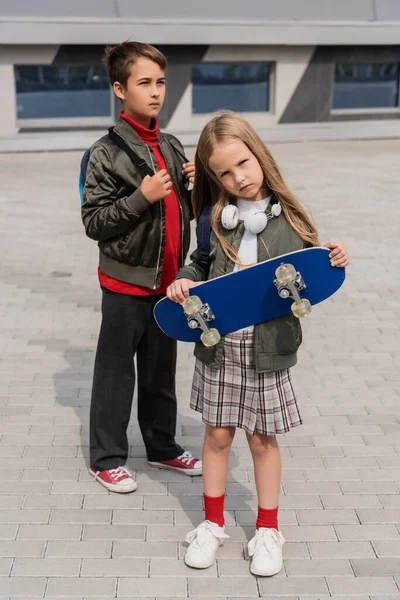 Full length of preteen kids in trendy bomber jackets standing with penny board outdoors — Stock Photo