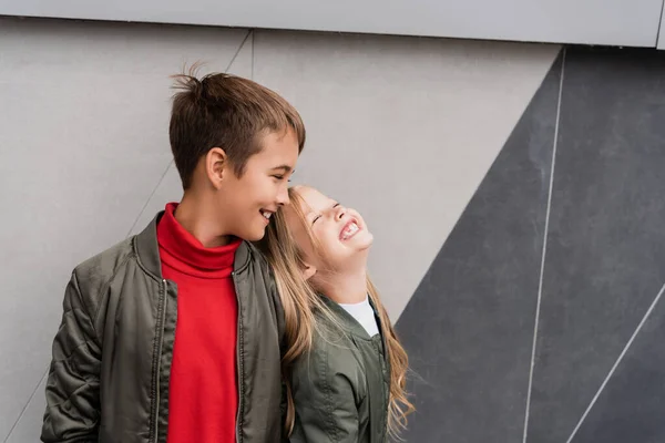 Happy and well dressed kids in bomber jackets smiling while standing near mall — Foto stock
