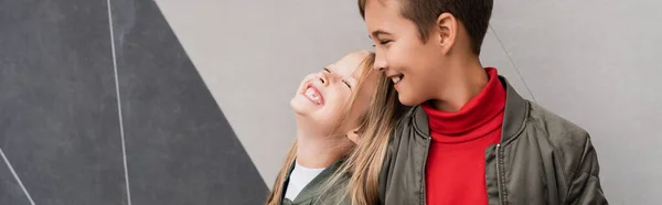 Счастливые и хорошо одетые дети в куртках бомбардировщика улыбаясь стоя возле торгового центра, баннер — стоковое фото