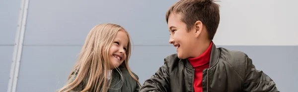 Happy preteen kids in bomber jackets looking at each other while standing near mall, banner - foto de stock