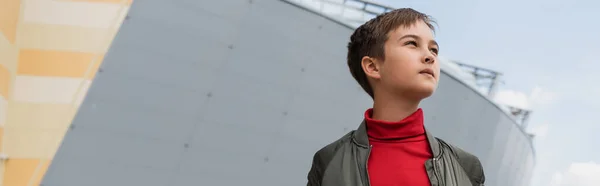 Well dressed preteen boy in stylish bomber jacket and red turtleneck looking away near mall, banner — Stockfoto