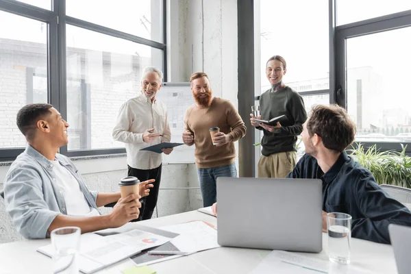 Gente alegre de negocios hablando con colegas interracial con portapapeles durante la formación en la oficina - foto de stock