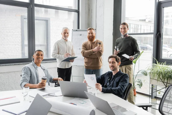 Lächelnde interrassische Geschäftsleute blicken während eines Treffens im Büro in die Kamera — Stockfoto
